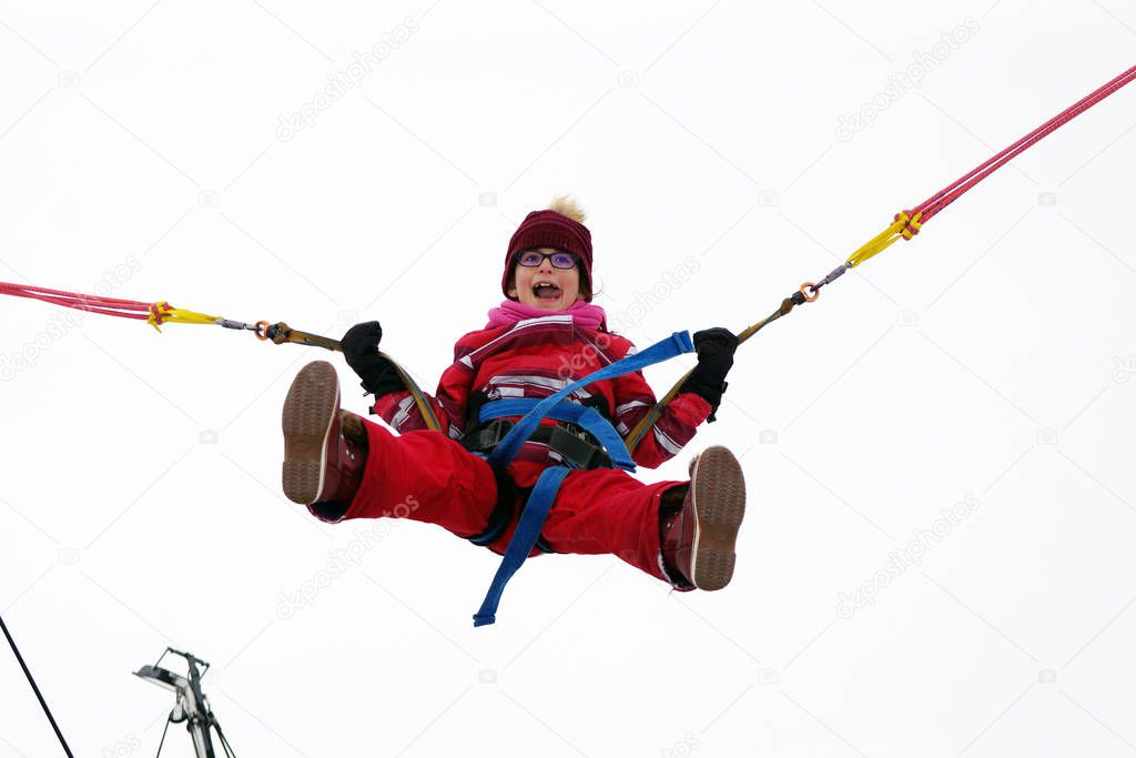 Little girl bungee jumping on trampoline during winter festival