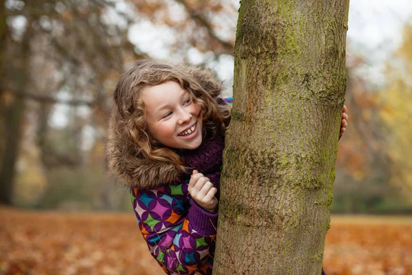 Lächelndes Mädchen versteckt sich hinter einem Baum — Stockfoto