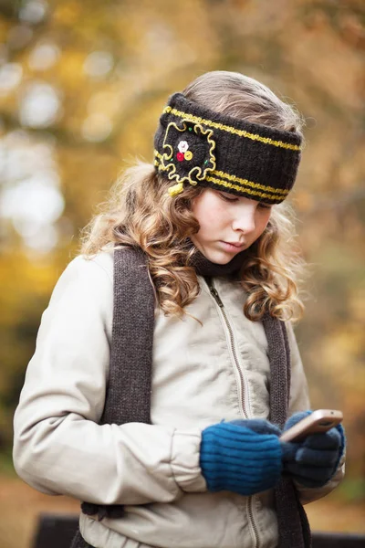 Menina mensagens de texto com celular em um parque de outono — Fotografia de Stock