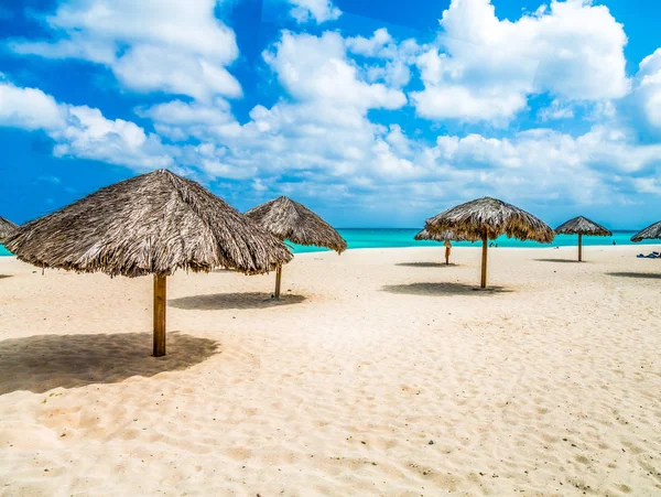 Na plaży Aruba przez parasole kryte strzechą — Zdjęcie stockowe