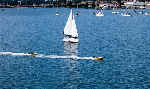 Biała żaglówka i żółte łodzie motorowe — Zdjęcie stockowe