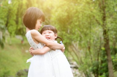 Oynama ve Bahçe park adlı sarılma kız kardeş. Asya aile açık havada dikey.