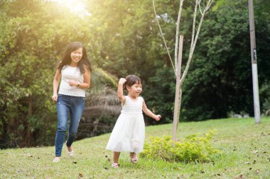Anne ve oynama ve yeşil park adlı çalışan küçük kız. Asya aile açık havada etkinlik.
