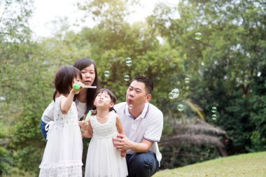 Asya aile açık havada etkinlik. Ebeveynler ve çocuklar yeşil park adlı sabun köpüğü üfleme. 