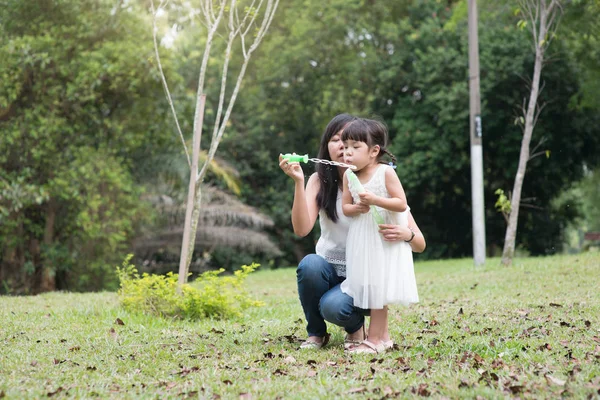 アジア家族野外活動 母と娘の緑豊かな公園でシャボン玉を吹く — ストック写真