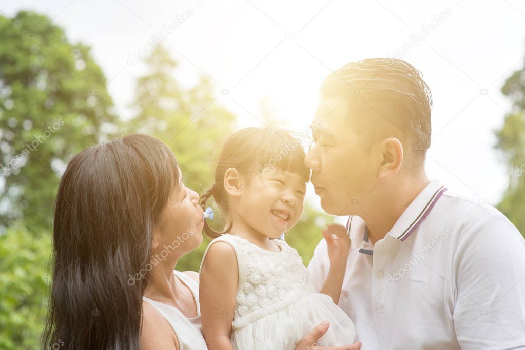 Parents kissing child at green park. Asian family outdoors activity.