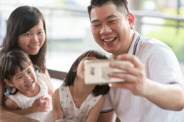 Happy Asian family taking selfie with smart phone at cafe. Outdoor lifestyle with natural light.