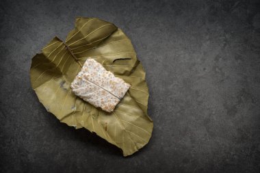 Koyu arkaplanda yaprağa sarılı taze çiğ tempeh. Üst görünüm.
