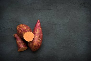 Koyu arkaplanda çiğ portakallı tatlı patatesler, fotokopi alanı ile üst görünüm.