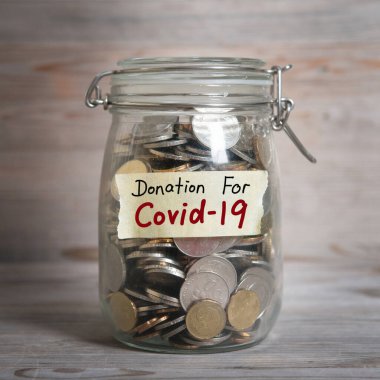Kovid19 etiketli cam para kavanozunda madeni paralar, finansal konsept. Dramatik ışıklandırmalı klasik ahşap arkaplan.