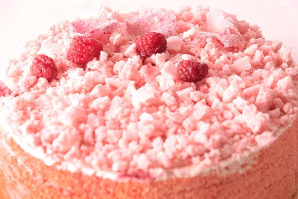 A pink cake covered with meringue crumbles, raspberries, and sugary rose petals.
