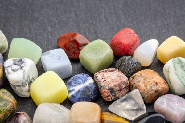 polished, semiprecious, colorful gemstones against gray slate stone with a copy space