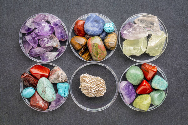 set of polished, semiprecious, colorful gemstones with Gypsum rosette (desert rose) in round bowls against a slate stone