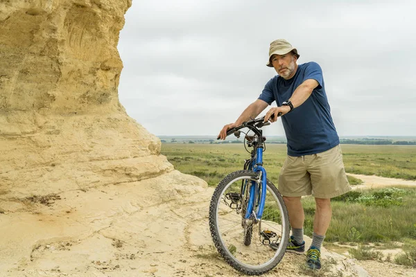 Senior male with a mountain bike at rock formations in Kansas prairie, summer scenery