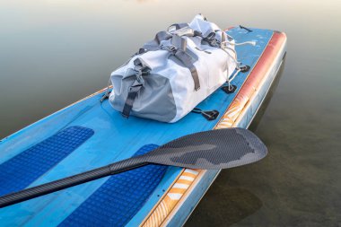 waterproof duffel on a deck of stand up paddleboard - paddling expedition concept clipart