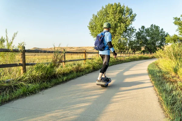 An adult man is riding an electric skateboard on the Poudre River Trail in northern Colorado.It is a  paved bike trail extending more than 20 miles between Timnath and Greeley.