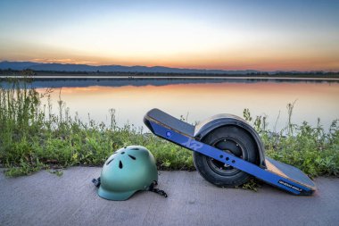Fort Collins, Co, Amerika Birleşik Devletleri - 11 Ağustos 2018: Onewheel elektrik kaykay bir göl günbatımı gökyüzü karşı hassas bir kask ile.