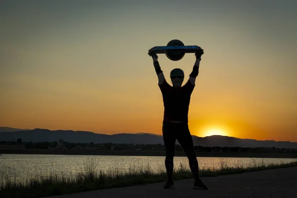 ロッキー山脈を越えて日没に対する彼の頭の上電気スケート ボードを握って男のシルエット — ストック写真