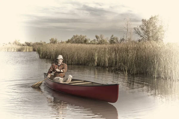 穏やかな湖でカヌーを漕ぐシニア男性カヌーを漕ぐ人レトロな Opalotype の調子を整える — ストック写真
