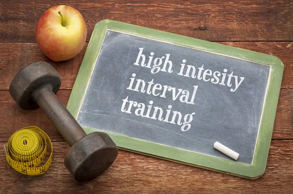 High intensity interval training  -  slate blackboard sign against rustic wood with a dumbbell, apple and tape measure