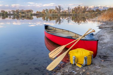 red tandem canoe with a wooden paddles and a dry bag on a lake shore, fall scenery in Colorado clipart