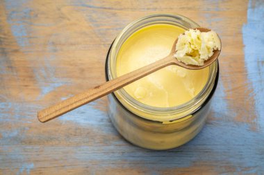jar and spoon of ghee (clarified butter) on grunge wood - top view clipart