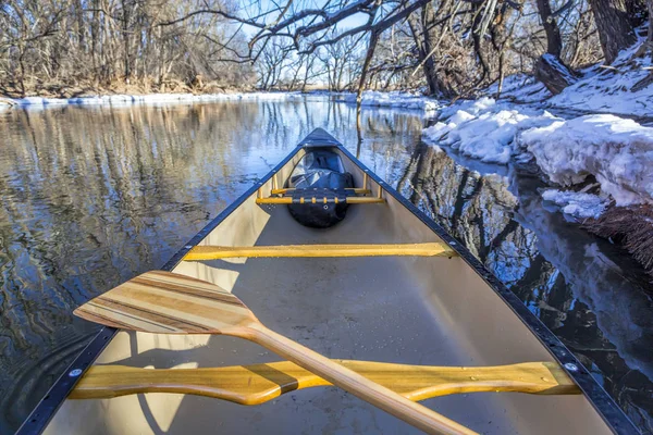 view from a canoe paddling on a river in winter scenery