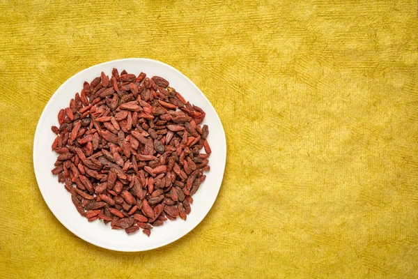 Dried Goji Berries White Plate Yellowtextured Paper Background Copy Space — Stock Photo, Image