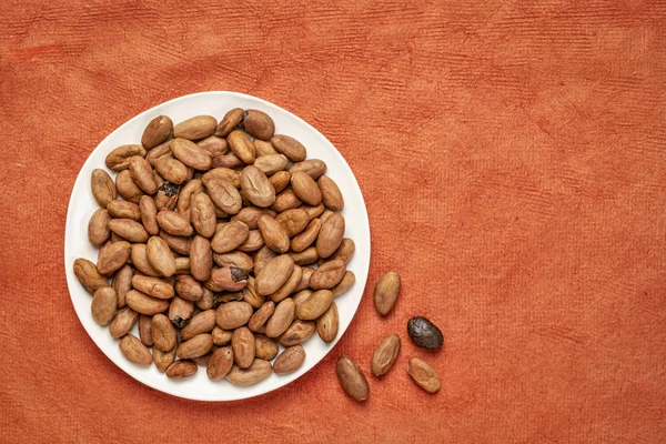 Rauwe Cacao Bonen Een Witte Plaat Tegen Achtergrond Van Rode — Stockfoto