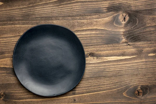 Черная тарелка на зернистой древесине — стоковое фото
