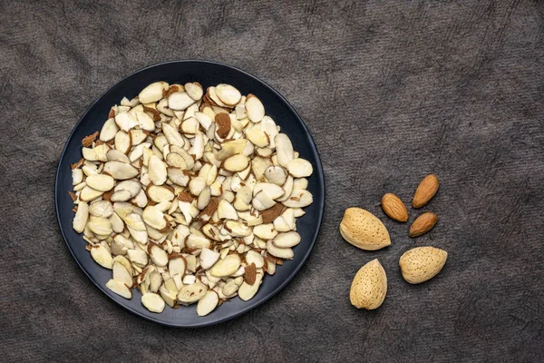 Almond slices and  nuts on a black plate — Stock Photo, Image