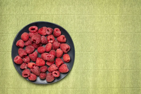 fresh red raspberries on black plate