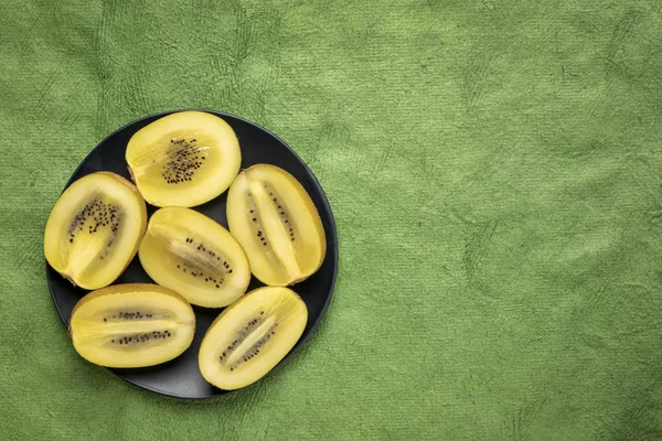 Cut gold kiwifruit berries on black plate — Stock Photo, Image