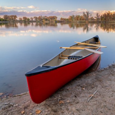 red tandem canoe with wooden paddles on a lake shore, fall scenery in Colorado