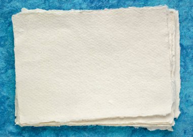 small sheet of blank white Khadi rag paper from South India against blue bark paper clipart