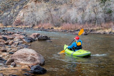 Kıdemli erkek kanocu, Fort Collins, Colorado 'nun yukarısındaki Poudre Nehri' ndeki bir dağ nehrinde şişirilebilir bir beyaz su kanosuyla kürek çekiyor.