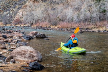 senior male kayaker  is paddling an inflatable whitewater kayak on a mountain river in early spring - Poudre River above Fort Collins, Colorado clipart