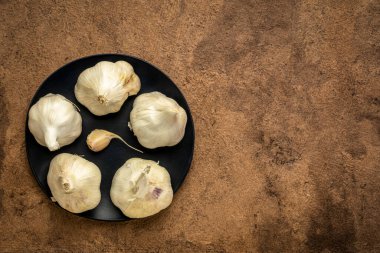 Siyah seramik bir tabakta sarımsak soğanları. Kabuk kağıdına karşı.