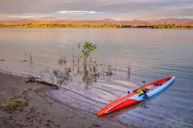 Kuzey Colorado 'daki Rocky Dağları' nın önünde, Boyd Gölü 'nün üzerinde gün doğumu. Kıyıda kürek çekmeye hazır uzun bir kürek çekme tahtasıyla.