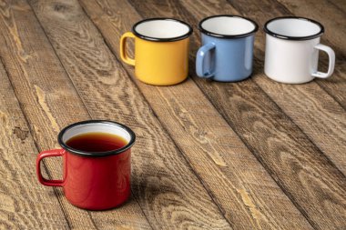 Kırsal ahşap piknik masasında kırmızı metal çay fincanı ve arka planda daha fazla bardak.