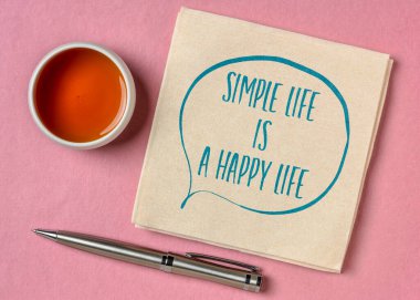 Basit hayat, mutlu bir hayattır. İlham verici bir alıntı. Bir bardak çay, mutluluk, başarı ve kişisel gelişim konseptiyle peçeteye yazılmış bir el yazısı.