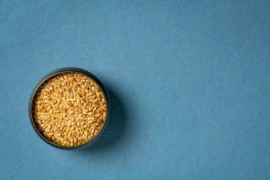 Küçük bir seramik kasede altın keten tohumu, fotokopi alanı, süper yiyecek takviyesi ve malzemesi olan mavi el yapımı kağıdın üst görüntüsü.