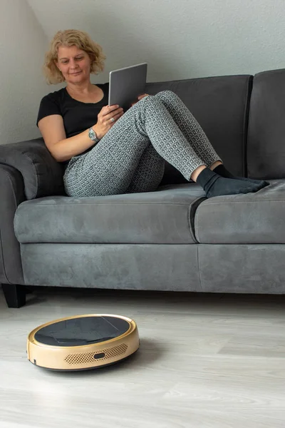 Женщина направляет своего робота пылесоса с дивана — стоковое фото