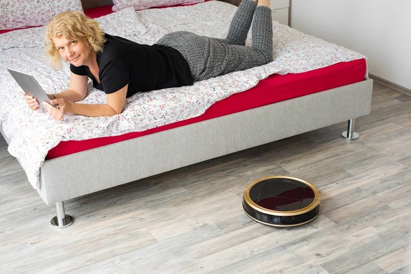 Vacuum cleaning robot with relaxed woman reading in the background — Stock Photo, Image