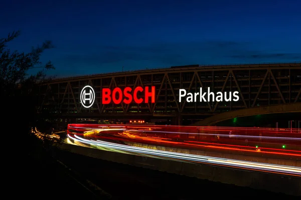 Enormes cartas de Bosch en el aparcamiento del aeropuerto de Stuttgart con larga exposición de la autopista A8 al atardecer. Bosch es una multinacional alemana de ingeniería y electrónica.. — Foto de Stock