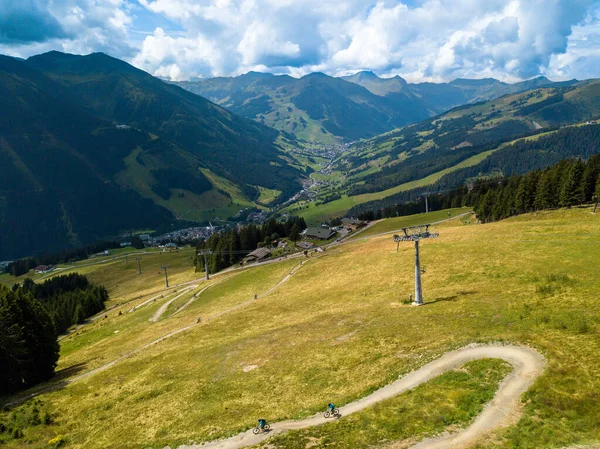 Motociclistas irreconocibles en un sendero de bicicleta de montaña en Saalbach en los Alpes austríacos en verano con teleférico en el fondo — Foto de Stock