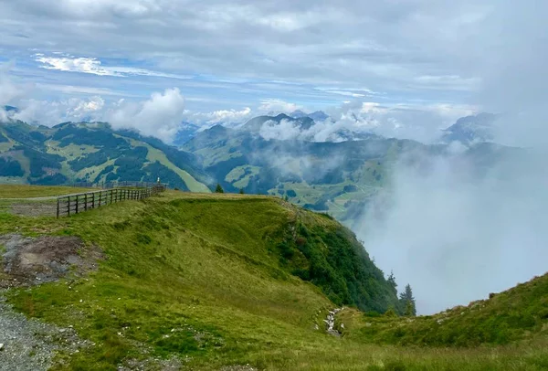 Uitzicht op de bergen in het skigebied Saalbach-Hinterglemm in Oostenrijk op een mooie zomerdag met laaghangende wolken en weelderige weiden die koeien gebruiken om te grazen — Stockfoto