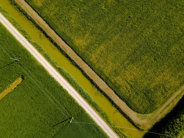 Imagem aérea de campos agrícolas com riachos, linhas de energia e faixas de sujeira em cores diferentes em forma geométrica como visto de cima usando um drone Imagens Royalty-Free
