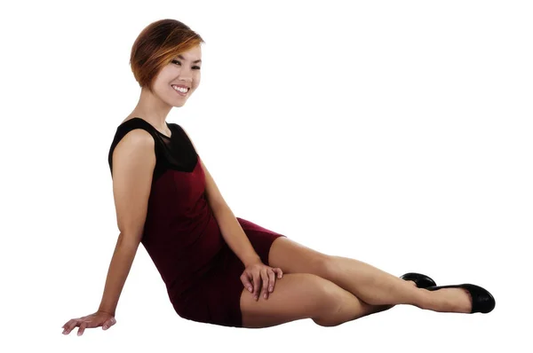 魅力的なアジア系アメリカ人女性の短い髪の赤いドレスに笑みを浮かべて白い背景の上に座って — ストック写真