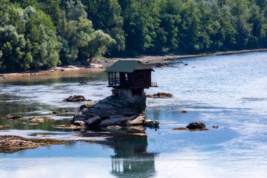 Small wooden cabin on a rock in the middle of river Drina, Serbia. clipart